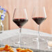 Two Acopa Silhouette wine glasses filled with red wine on a table with food.