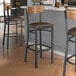 A Lancaster Table & Seating bar stool with a dark brown vinyl seat and vintage wood back next to a counter.