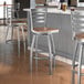 A Lancaster Table & Seating swivel bar stool with a wooden seat at a table in a bar.
