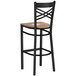 A Lancaster Table & Seating black cross back bar stool with a wooden seat.