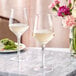 Two Acopa Silhouette wine glasses filled with white wine on a marble counter.