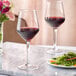 Two Acopa Silhouette wine glasses filled with red wine on a marble table with a plate of food.