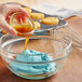 A person pouring LorAnn Preserve-It Natural Antioxidant into a bowl of blue frosting.