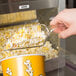 A hand using a Carnival King clear plastic utility scoop to serve popcorn.