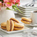 A white plate with three White Toque French caramel macarons and a cup of coffee on a table.