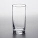 An Arcoroc beverage glass filled with a clear liquid on a white surface.