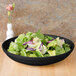A CAC Festiware black bowl filled with salad on a table.