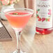 A glass of Monin Premium strawberry rose syrup mixed with a pink liquid and garnished with a green leaf.