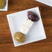 Three WNA Comet white square dishes with olives and cheese on a table.