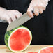 A person in a plastic glove cutting a watermelon with a Dexter-Russell Santoku knife.