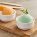 Two Tablecraft white mini melamine bowls with ice cream scoops of green and orange ice cream.