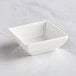 A Tablecraft white square melamine bowl on a white surface.