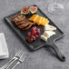 A Tablecraft rectangular faux slate melamine serving paddle with cheese, grapes, and crackers on it.