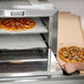 A man using a Nemco countertop pizza oven to cook a pizza.