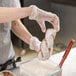 A person in a white apron preparing a Rich's twisted yeast donut with white frosting.