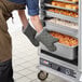 A person in an apron using oven mitts to open a clear door on a ServIt holding and proofing cabinet.
