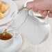 A hand pouring tea into a white Tuxton teapot.