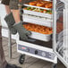 A person in green oven mitts using a ServIt holding cabinet with clear door to put food in a tray.