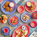 An outdoor table set with Acopa Foundations orange narrow rim melamine plates and bowls of food.