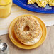 A bagel with a cream cheese spread on a yellow Acopa Foundations melamine plate.