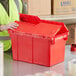 A woman in a vest opening a red Orbis Stack-N-Nest Flipak tote box.