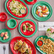 A table with Acopa Foundations green melamine plates of food, including a plate of salad with red sauce on it.