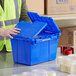 A man in a safety vest opening a dark blue Orbis Stack-N-Nest Flipak tote box with a hinged lid.