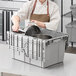 A woman in a chef's uniform holding a gray Orbis Stack-N-Nest Flipak tote box with a hinged lid.