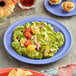 A purple Acopa Foundations melamine plate of guacamole with tomatoes and tortilla chips on a table.