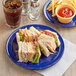 A plate of sandwiches and fries with a drink on a table with an Acopa blue melamine plate of sandwiches and a drink.