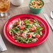 A red Acopa Foundations melamine plate with salad and pasta on a table.