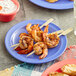 A purple Acopa Foundations melamine plate with grilled shrimp and white sauce on a table.