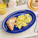 An Acopa blue melamine oval platter with scrambled eggs and toast on a table.