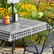 A table with a black gingham vinyl table cover and umbrella opening on a patio.