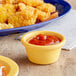 A yellow Acopa Foundations ramekin of ketchup next to a plate of fried shrimp.