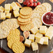 A plate with Nabisco assorted entertainment crackers, cheese, and grapes on a table at a catering event.