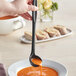 A person holding a Tablecraft black silicone-coated stainless steel ladle over a bowl of soup.