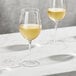 Two Della Luce Maia wine glasses filled with white wine on a marble table.