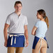 A man and woman standing next to each other wearing Choice royal blue waist aprons with natural webbing.