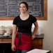 A woman wearing a red Choice waist apron with black trim over a black shirt standing in front of a chalkboard.