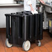 A person in a white coat placing a white plate in a black Cambro dish caddy.