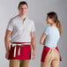 A man and woman wearing red poly-cotton waist aprons with natural webbing and 3 pockets.