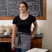 A woman wearing a gray Choice poly-cotton waist apron with black webbing and 3 pockets.