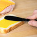 A Sabert black plastic spreader being used to spread butter on a piece of bread.