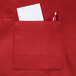 A red Chef Revival bib apron with a pocket holding a pen and paper.