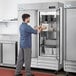 A man opening the white door of an Avantco A Plus stainless steel reach-in freezer.