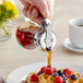 A person using a Vollrath clear glass syrup server to pour syrup over a waffle with berries.