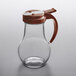 A glass syrup dispenser with a brown lid and handle.