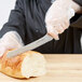 A person in gloves using a Dexter-Russell Basics offset bread and sandwich knife to cut a loaf of bread.