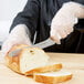A person in gloves using a Dexter-Russell serrated knife to cut bread on a counter.